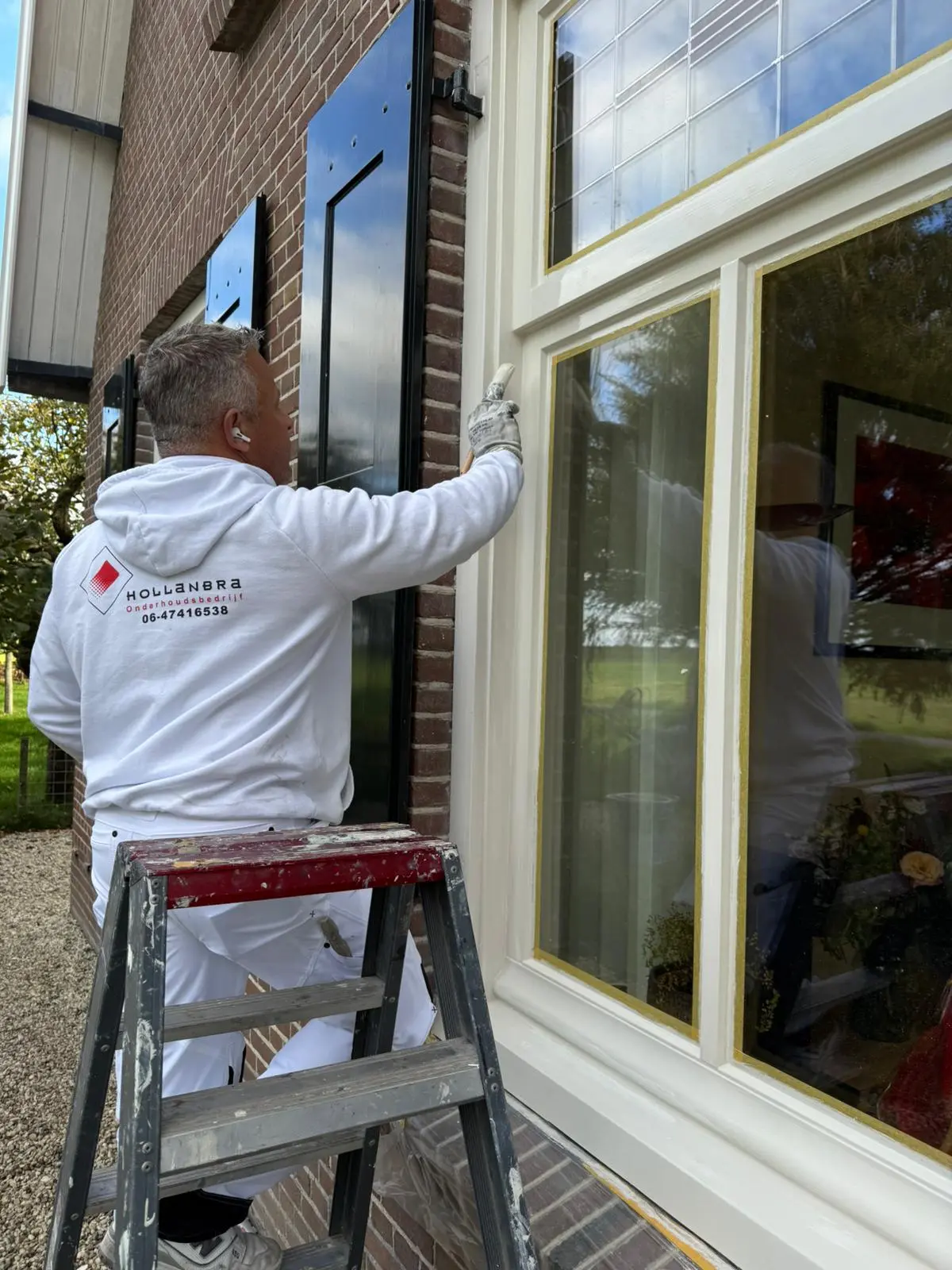 Vakman van Hollanbra schildert een houten kozijn aan de buitenzijde van een woning