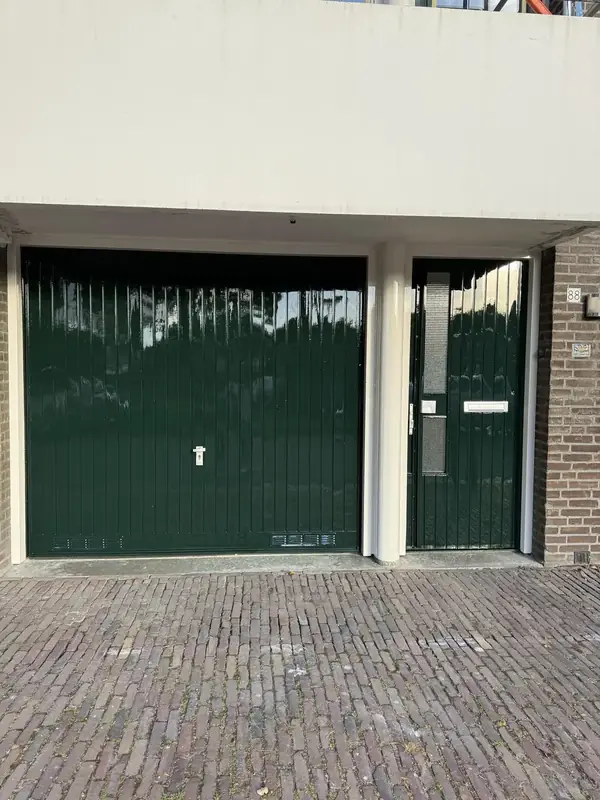 Donkergroene garagedeur en voordeur onder een wit balkon