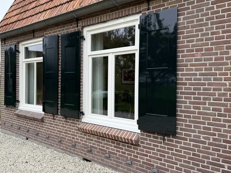 Wit kozijn met zwarte luiken in een bakstenen gevel, close-up