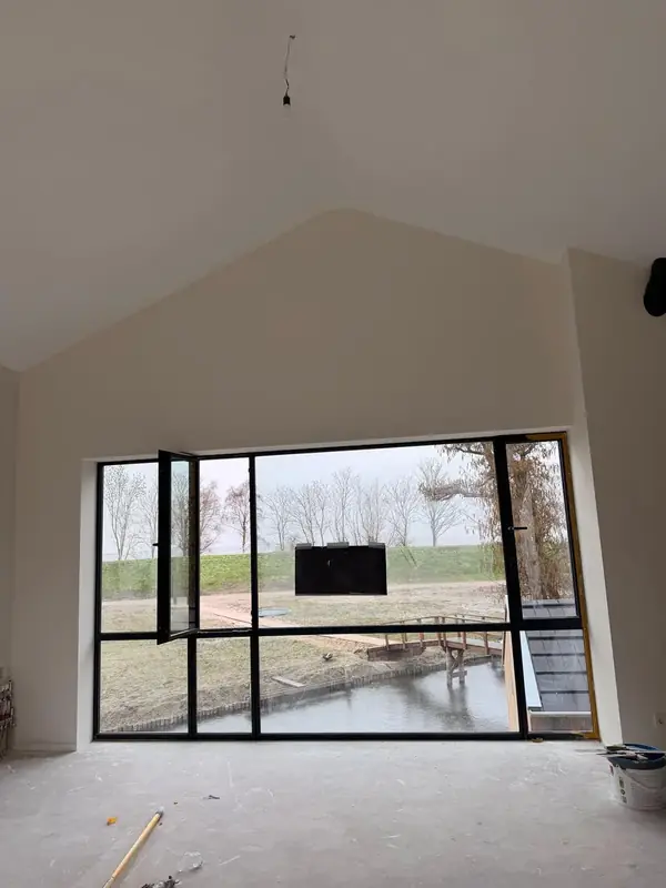 Ruime lichte kamer met hoog plafond, wit afgewerkte muren en groot raam