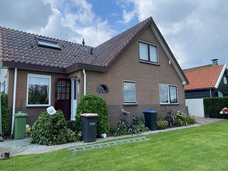 Woning met bakstenen gevel en een bordeauxrode voordeur, gezien vanuit de tuin