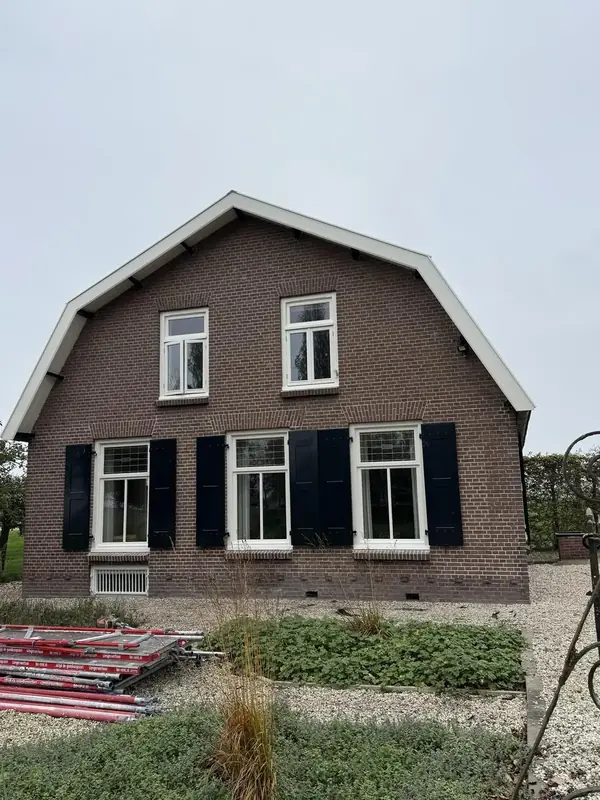 Woning met bakstenen gevel, witte kozijnen en zwarte luiken